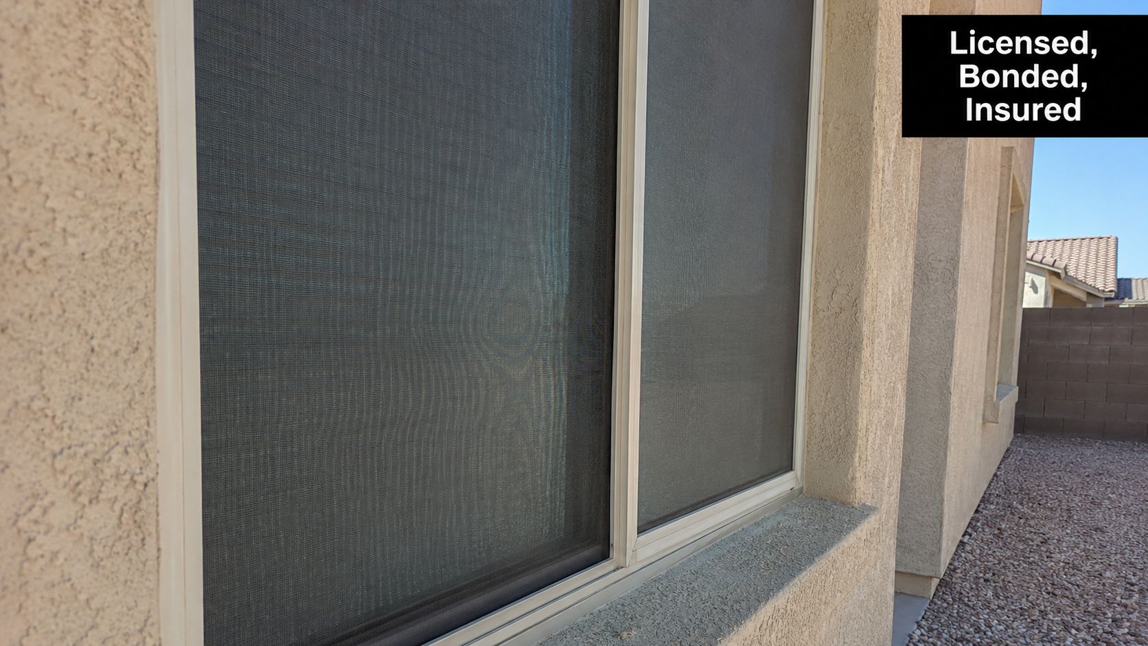 A close-up view of dark solar sun screens installed on residential windows of a stucco house.