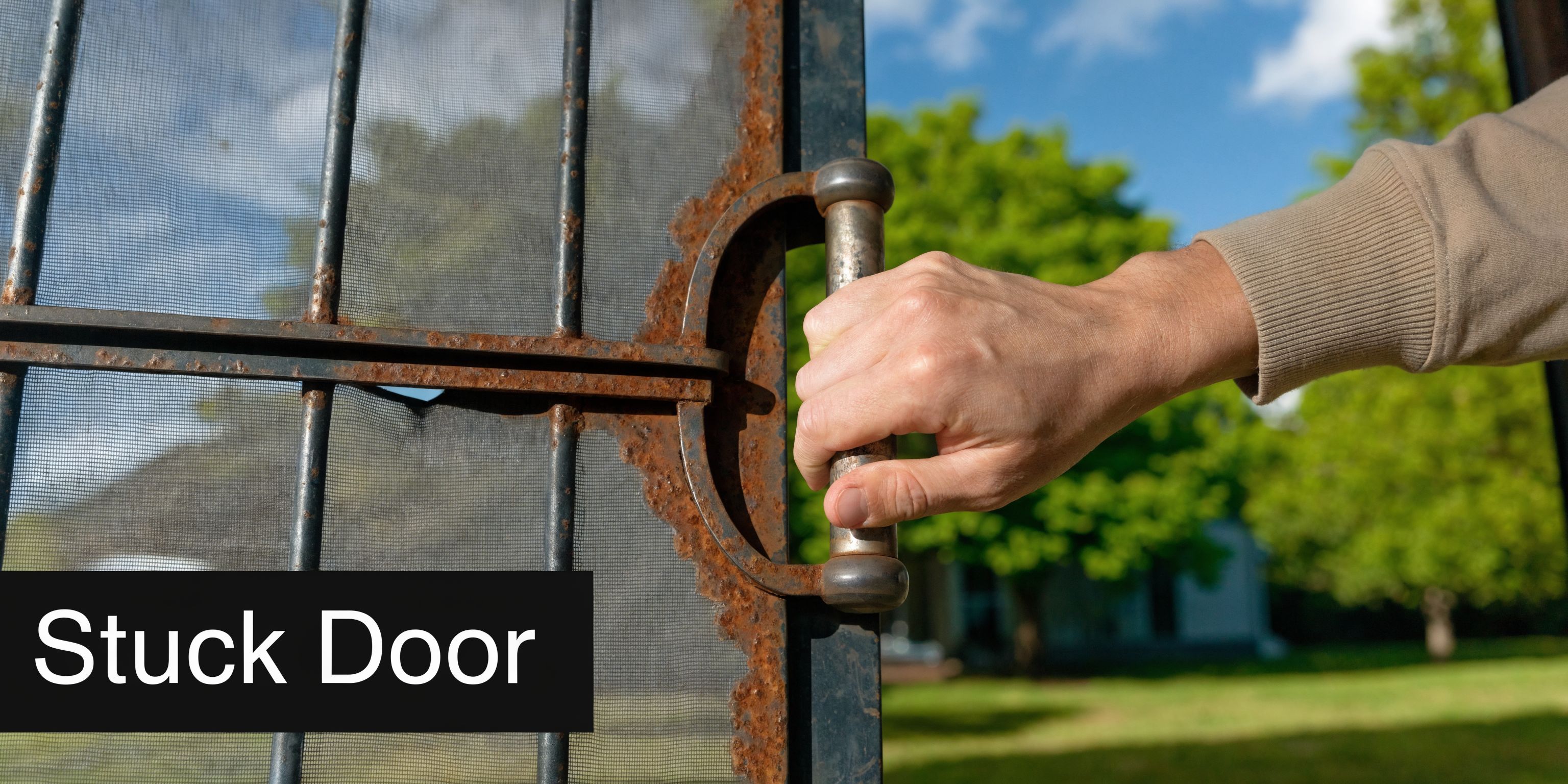 A close-up of a hand gripping a rusty metal screen door handle that is stuck.