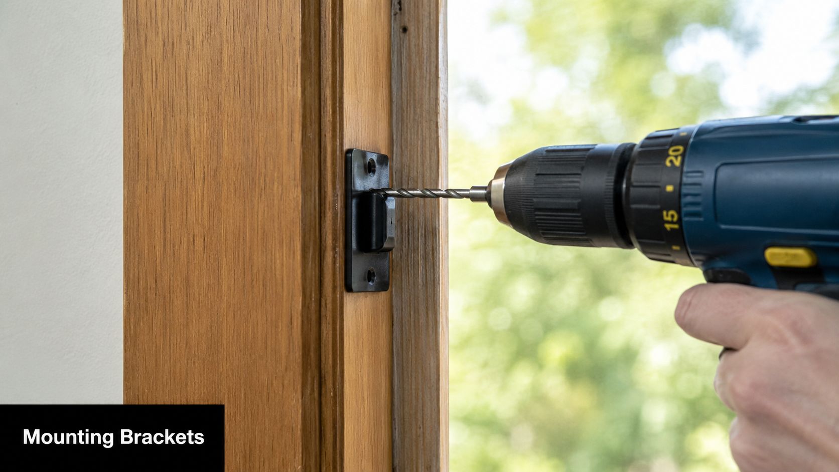 A hand using a cordless power drill to screw a black mounting bracket into a wooden frame.