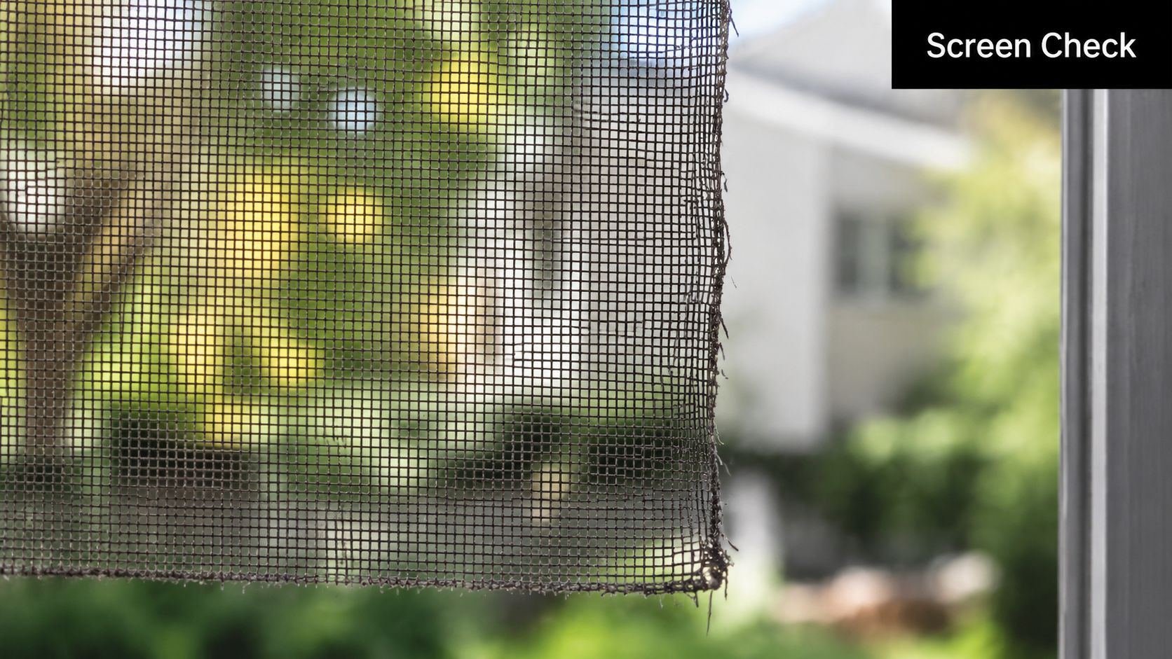 A close up view of a torn window screen looking out towards a blurry green residential backyard.